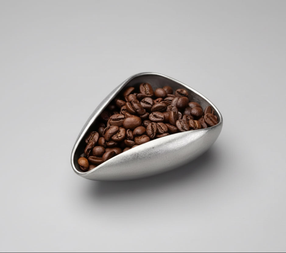 Triangular metal container filled with coffee beans on a gray surface